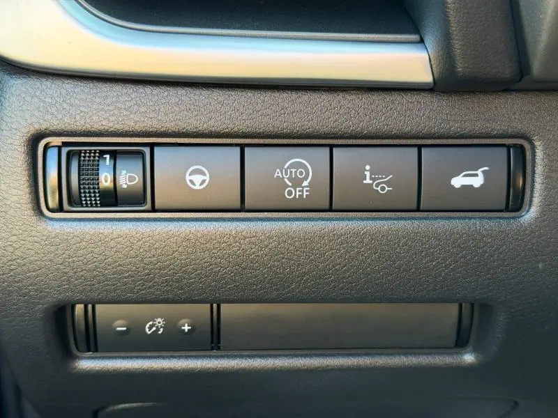 Gros plan sur les commandes noires du tableau de bord du Nissan Qashqai 2025, avec réglage phares et ouverture coffre.