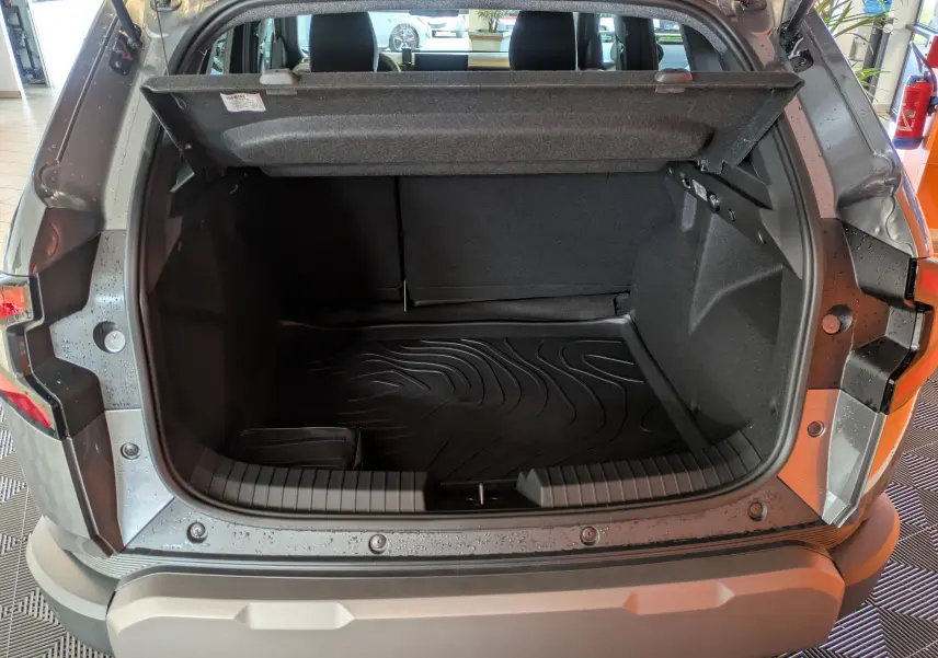 Coffre ouvert du Dacia Duster 1.6 Hybrid 140 Extreme gris schiste, vue arrière montrant l'espace de chargement et le tapis de protection.
