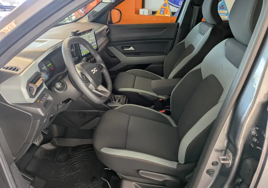Vue intérieure côté conducteur du Dacia Duster 1.6 Hybrid 140 gris schiste, avec sièges bi-ton et tableau de bord moderne.