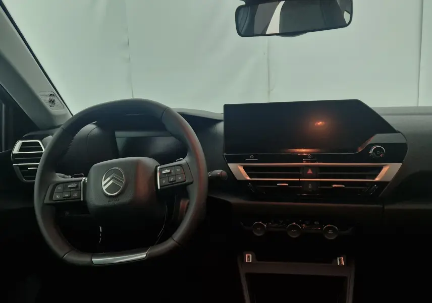 Intérieur de la Citroën C4 2025, vue frontale du tableau de bord avec volant cuir et écran tactile central noir.
