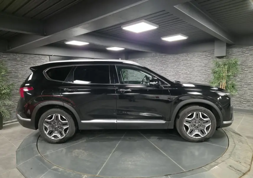 Profil côté gauche du Hyundai Santa Fé 2023 noir métallisé avec jantes alliage et vitres surteintées en intérieur showroom.