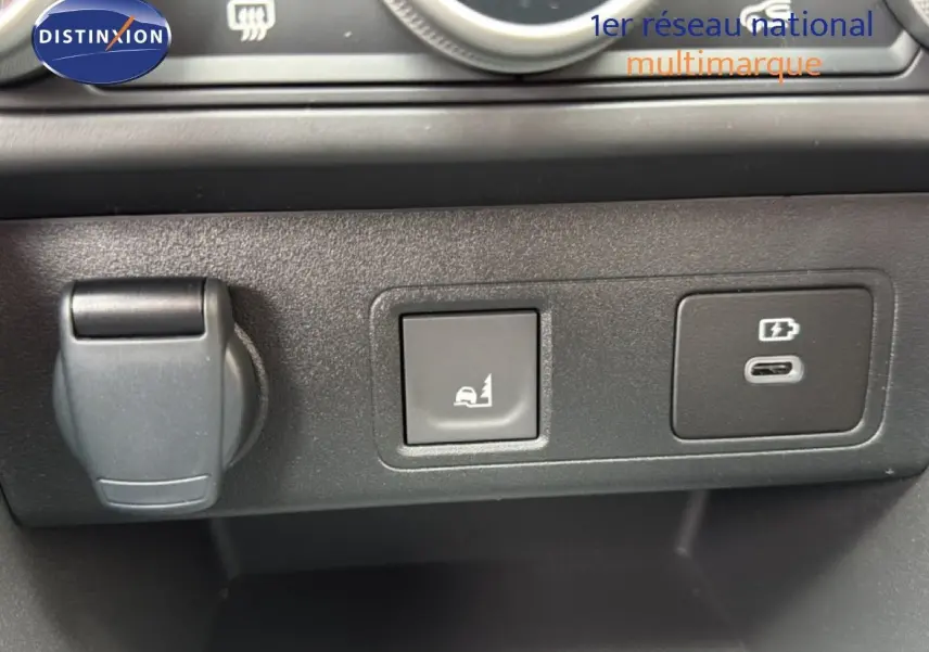 Détail intérieur montrant une prise 12V, un bouton d'assistance en côte et un port USB-C sur tableau de bord noir.