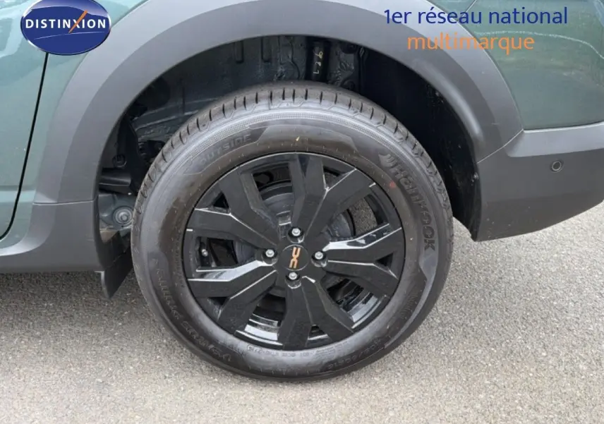 Gros plan sur la roue arrière droite noire avec jante noire brillante du Dacia Jogger vert cèdre métal.