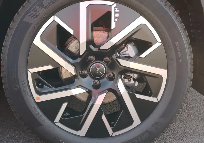 Gros plan sur la jante noire et argentée du Jeep Compass 2026 en Noir Vulcano Metal, mettant en valeur le logo central.