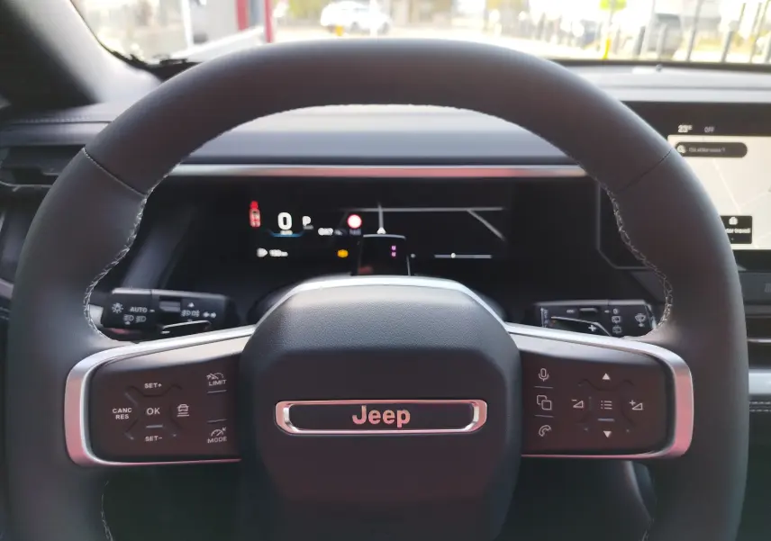Vue rapprochée du volant noir du Jeep Compass 2026, avec commandes intégrées et tableau de bord numérique en arrière-plan.
