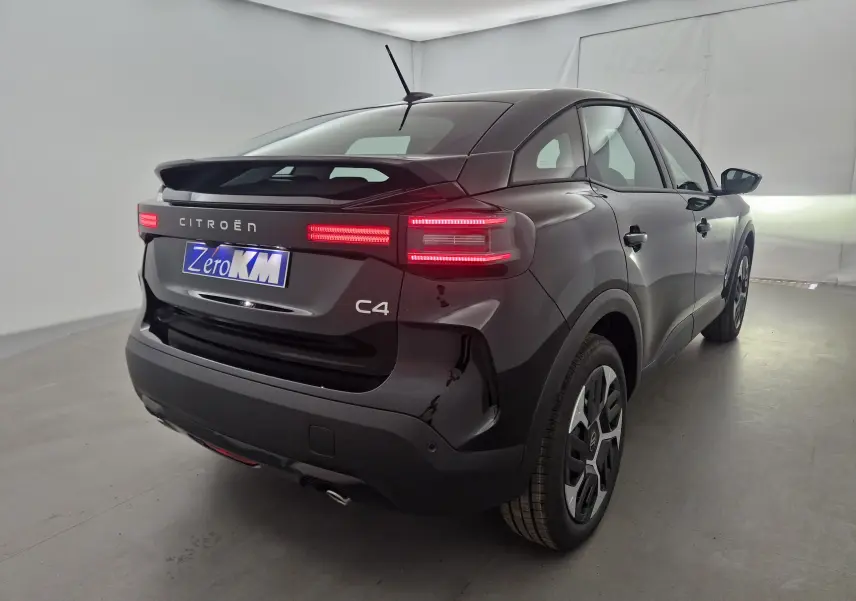 Vue 3/4 arrière droite d'une Citroën C4 noire 2025 avec feux arrière LED allumés dans un studio blanc.