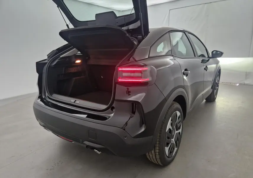 Vue 3/4 arrière droite d'une Citroën C4 noire 2025 avec coffre ouvert et feux arrière allumés dans un studio.