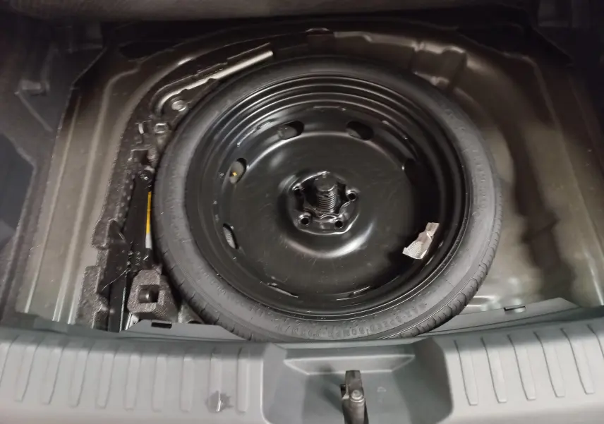 Roue de secours en acier noir dans le coffre d'une CUPRA Leon Ph.2 1.5 eTSI 150 DSG7 avec espace de rangement autour.