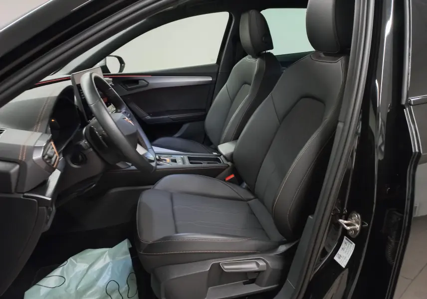 Vue intérieure côté conducteur de la CUPRA Leon 2025 noir minuit, sièges en cuir avec surpiqûres cuivrées et tableau de bord moderne.