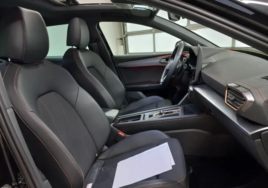 Intérieur avant droit de la CUPRA Leon 2025 noir Minuit, sièges cuir noirs avec surpiqûres cuivrées et toit ouvrant panoramique visible.