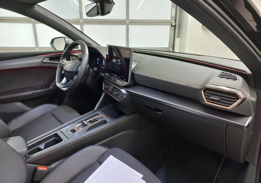 Vue intérieure côté conducteur de la CUPRA Leon 2025 noire avec tableau de bord moderne et éclairage d'ambiance cuivré.