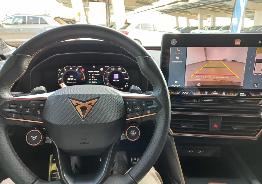 Vue intérieure du poste de conduite de la CUPRA Leon 2025 avec volant noir et écran tactile affichant la caméra de recul.