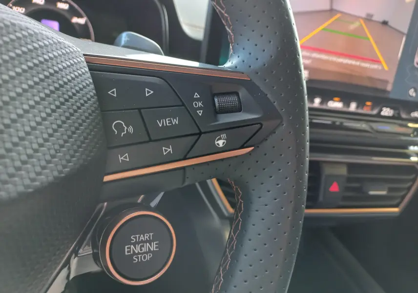 Gros plan sur le volant perforé et les commandes cuivrées d'une CUPRA Leon 2025 avec tableau de bord et écran de recul.