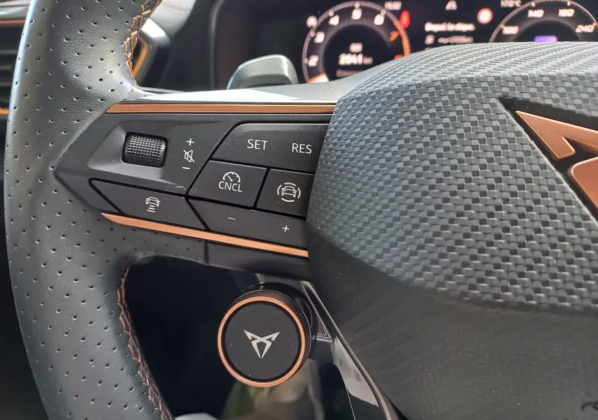Gros plan sur le volant perforé noir avec surpiqûres cuivrées et commandes multifonctions du CUPRA Leon 2025.