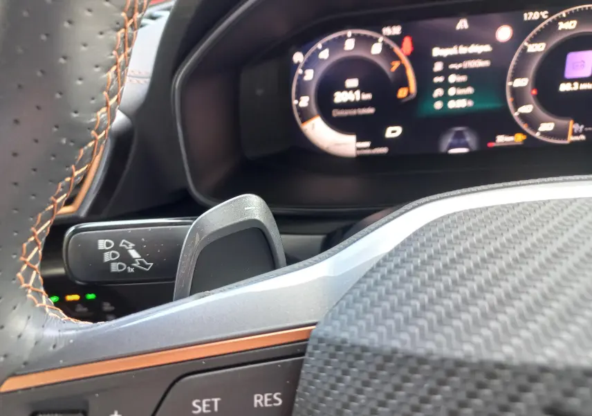 Gros plan sur le volant en cuir noir avec surpiqûres cuivrées et le tableau de bord numérique du CUPRA Leon 2025.