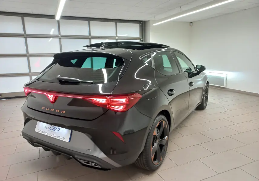 Vue 3/4 arrière droite d'une CUPRA Leon 2025 noir minuit avec toit ouvrant panoramique et jantes cuivrées 18 pouces.