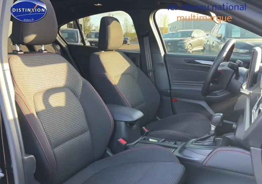 Vue intérieure avant droite de la Ford Focus noire 2024 avec sièges tissu noir et surpiqûres rouges, console centrale et volant cuir.