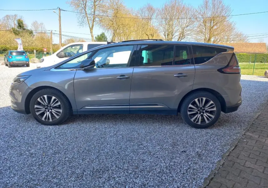 Vue de profil côté gauche d'un Renault Espace gris 2017 garé sur un sol gravillonné, avec jantes alliage et vitres teintées.