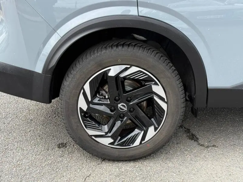 Gros plan sur la roue avant droite du Nissan Qashqai gris Argile avec jante alliage noire et argentée au design moderne.