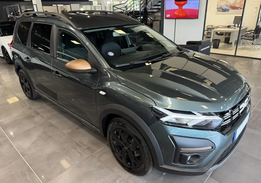 Dacia Jogger Hybrid 140 Extreme vert cèdre en 3/4 avant droit avec rétroviseurs bronze et jantes noires en showroom.