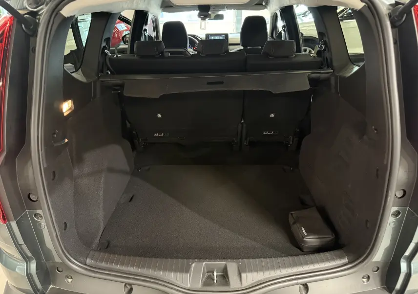 Coffre ouvert vu de l'arrière d'une Dacia Jogger Hybrid 140 Extreme vert cèdre, montrant l'espace de chargement et la banquette arrière.