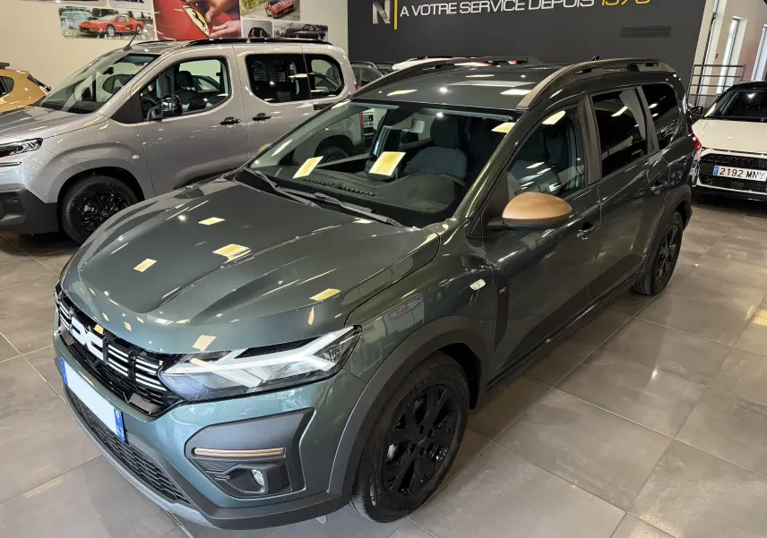 Vue 3/4 avant droite d'une Dacia Jogger Hybrid 140 Extreme vert cèdre avec rétroviseurs couleur bronze et jantes noires en showroom.