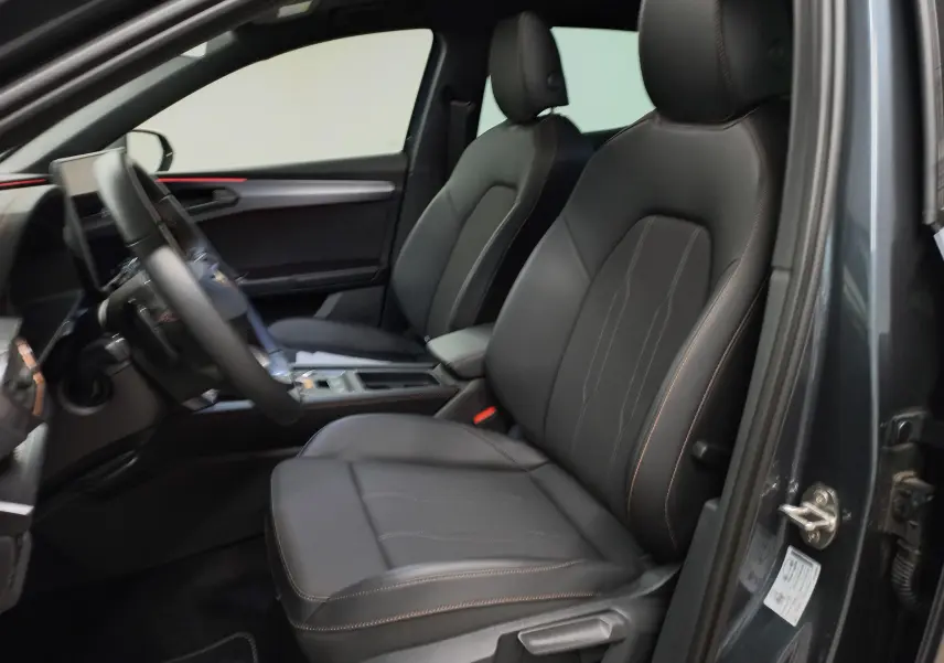 Intérieur avant droit d'une CUPRA Leon gris magnétique, sièges noirs avec surpiqûres cuivrées et tableau de bord moderne.