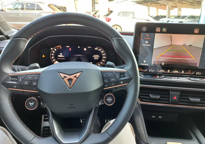 Vue intérieure centrée sur le volant CUPRA avec commandes, tableau de bord numérique et écran multimédia affichant la caméra de recul.