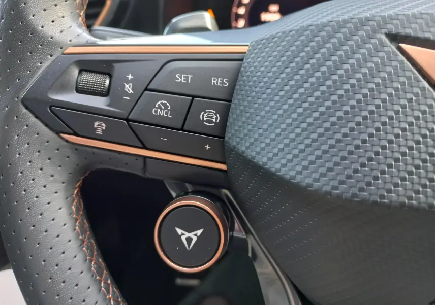 Gros plan sur le volant perforé noir avec surpiqûres cuivrées et commandes multifonctions du CUPRA Leon 2025