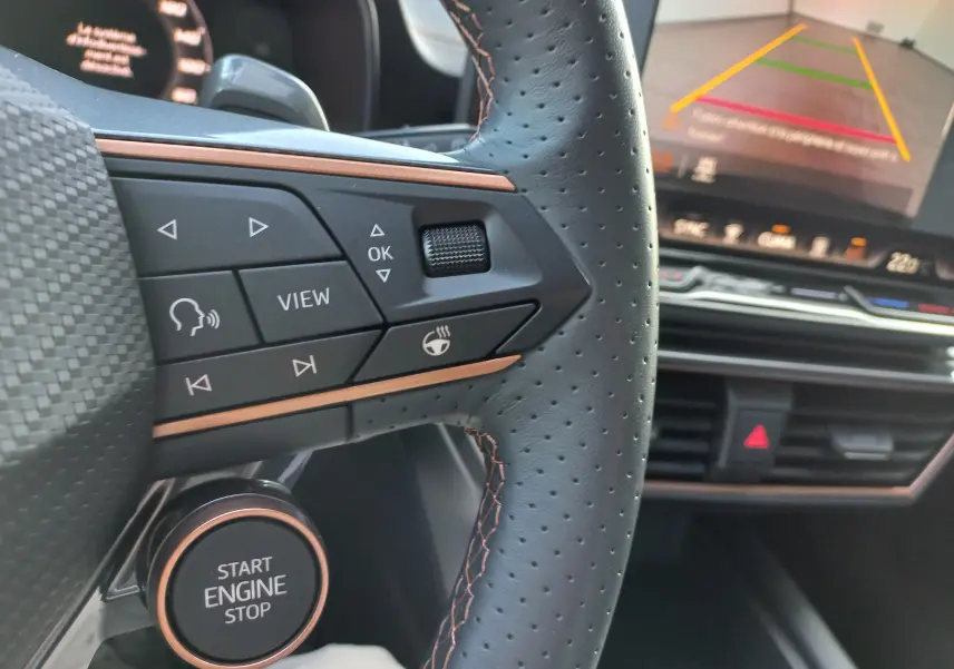 Gros plan sur le volant perforé et les commandes cuivrées d'une CUPRA Leon 2025 avec tableau de bord et écran de recul.