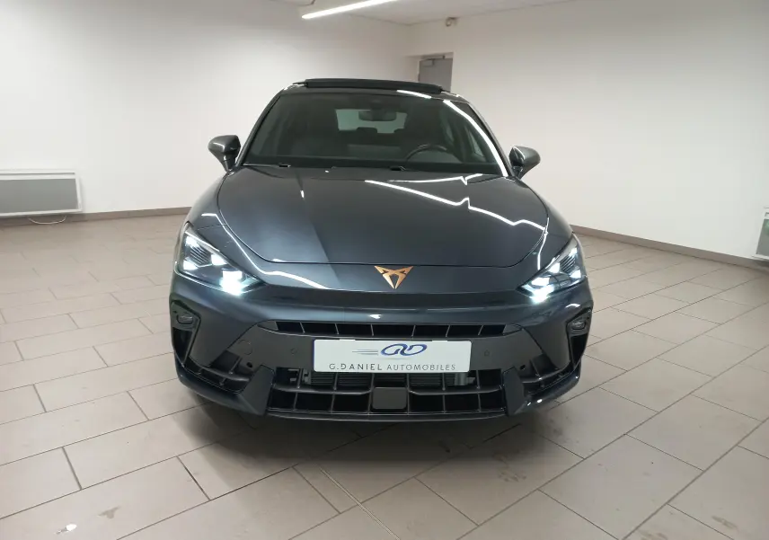 Vue de face d'une CUPRA Leon 2025 gris magnétique avec logo cuivré et phares LED allumés en intérieur.