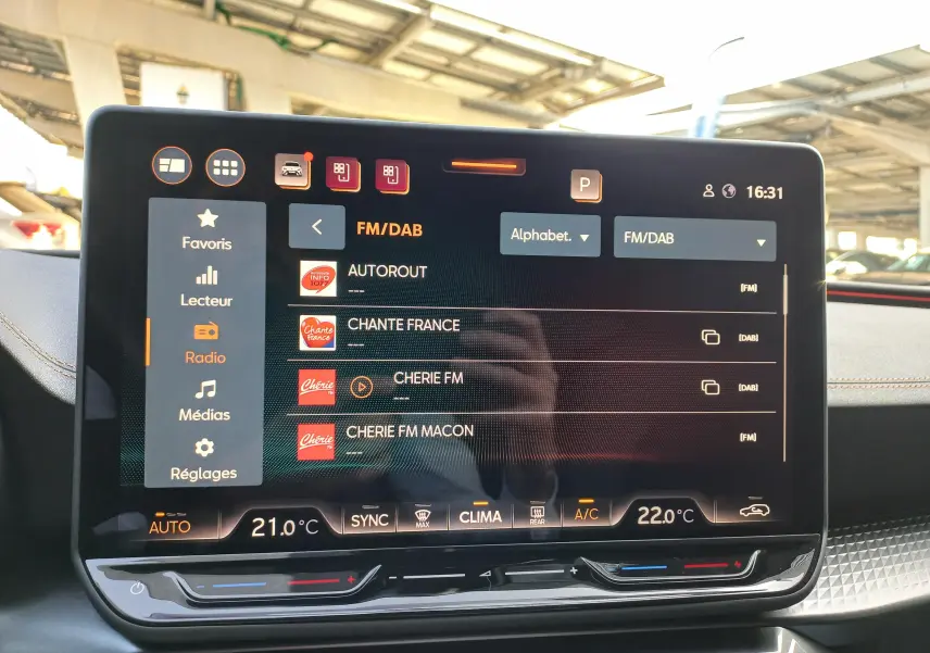 Écran tactile central de la CUPRA Leon 2025 affichant les stations radio FM/DAB avec commandes climatisation en dessous.