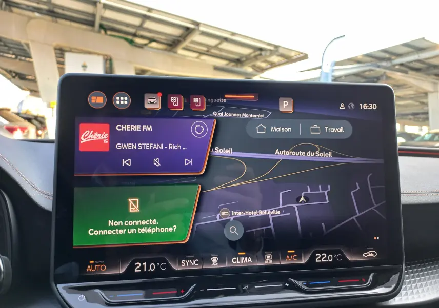 Écran central tactile du tableau de bord du CUPRA Leon 2025 affichant navigation et radio, ambiance intérieure noire avec surpiqûres cuivrées.