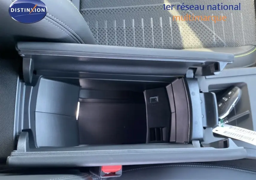 Vue plongeante sur le rangement central ouvert d'une Peugeot 308 Hybrid blanche, avec clé et sellerie noire visible.