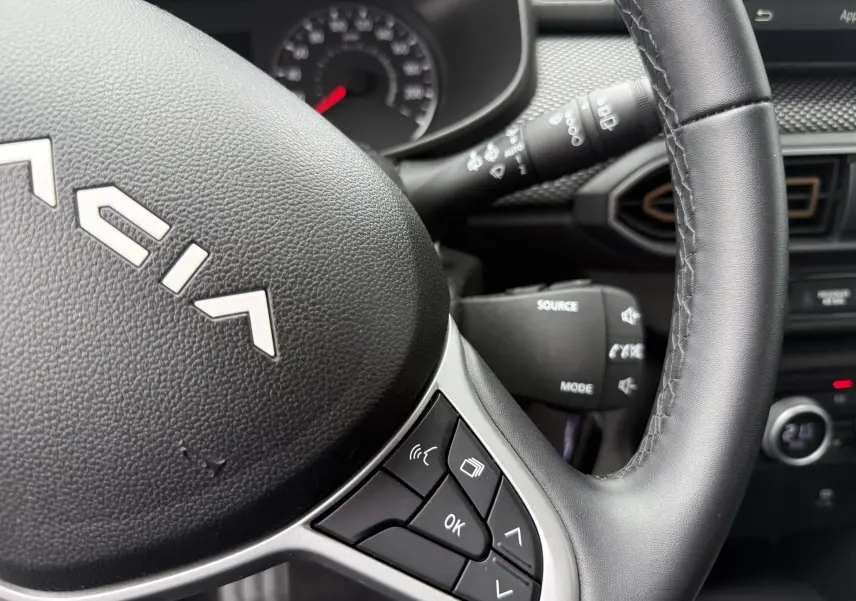 Gros plan sur le volant noir du Dacia Sandero Stepway 2025 avec commandes intégrées et tableau de bord partiellement visible.