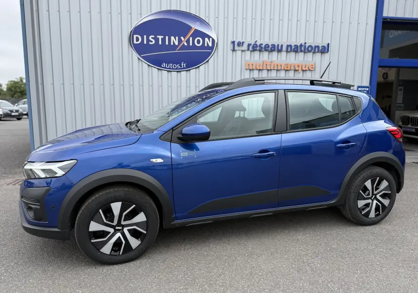Vue de profil côté gauche d'une Dacia Sandero Stepway 2025 bleu iron avec jantes spécifiques et barres de toit noires.