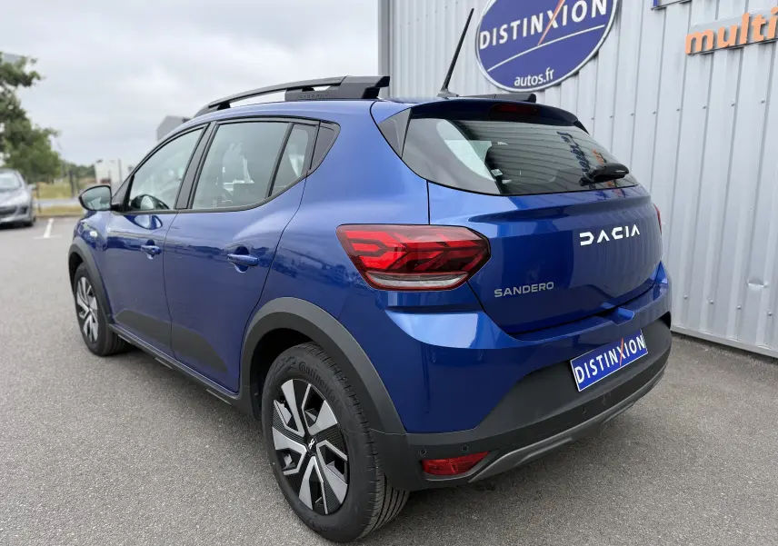 Vue 3/4 arrière droite d'une Dacia Sandero Stepway bleu iron 2025 avec feux arrière LED et barres de toit noires.