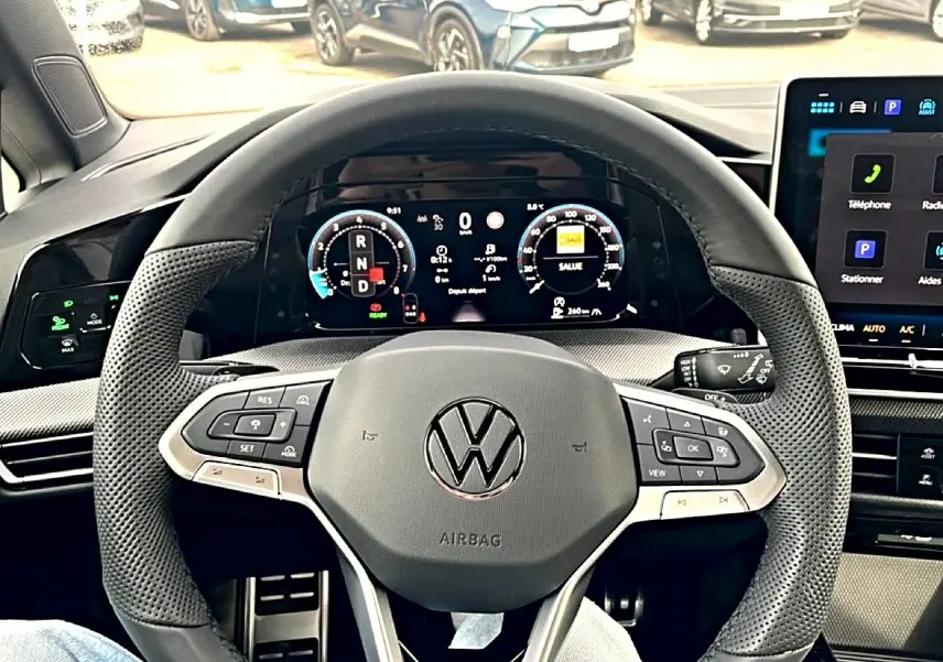 Vue intérieure centrée sur le volant cuir perforé et l'écran numérique du tableau de bord de la Volkswagen Golf noire 2026.