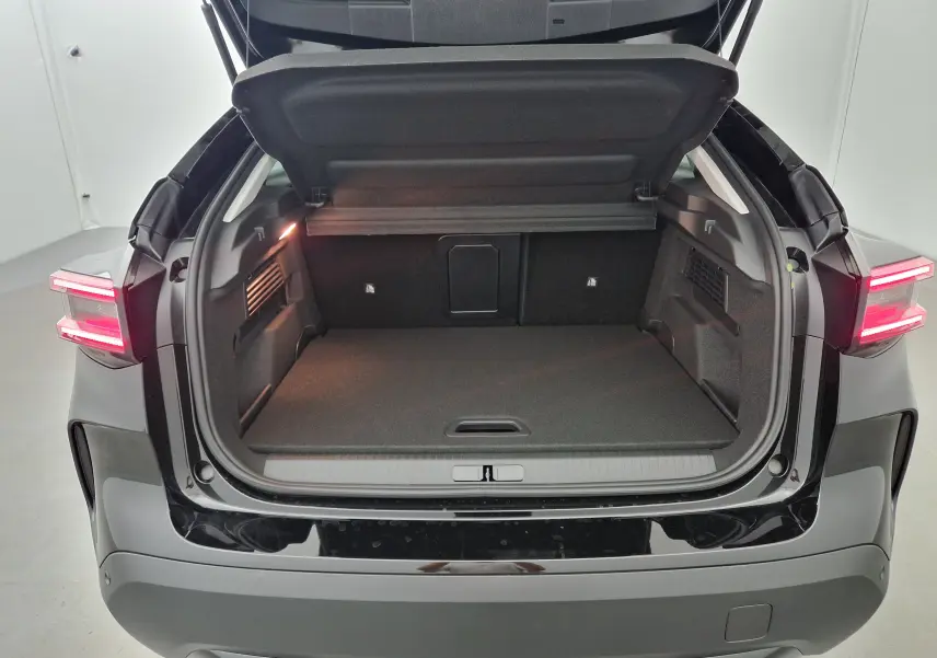 Coffre ouvert vu de l'arrière d'une Citroën C4 1.2 HYBRID 136 e-DSC6 MAX noire avec feux arrière allumés.