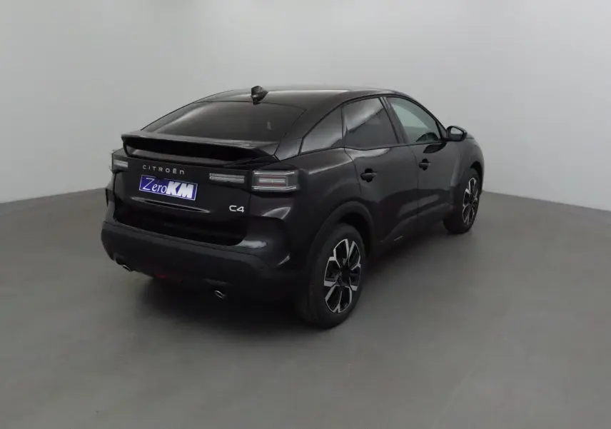 Vue 3/4 arrière d'une Citroën C4 noire 2025 avec toit incliné et jantes noires à motifs argentés.