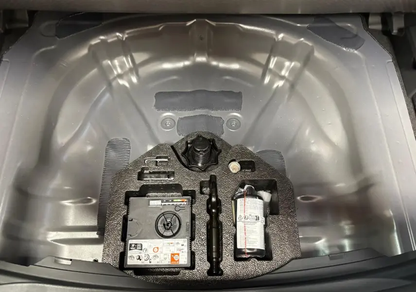 Vue plongeante sur le coffre ouvert d'une CUPRA Leon 2025, montrant le rangement métallique gris et les outils intégrés.