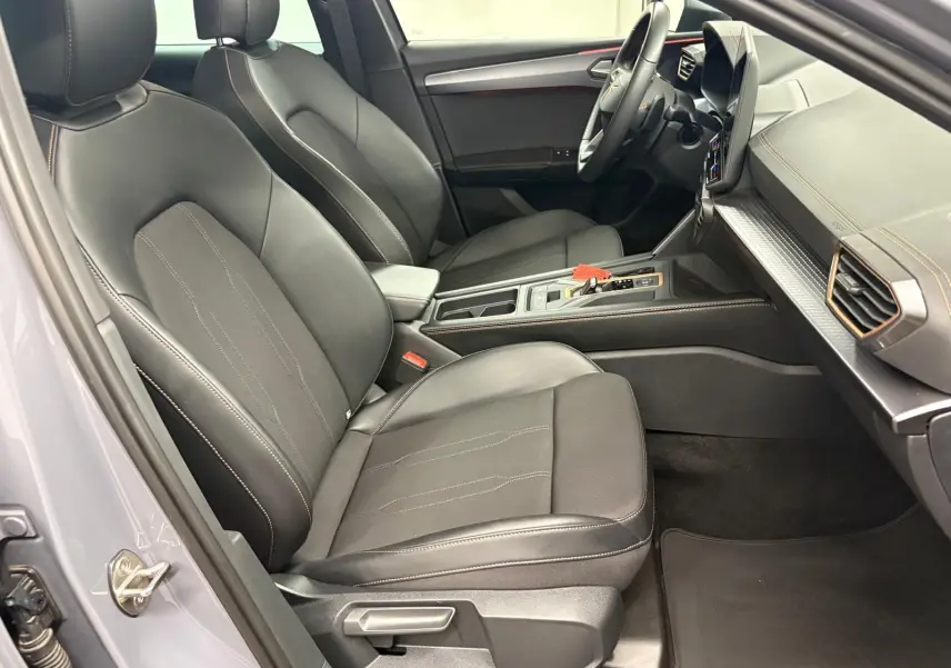 Vue intérieure côté conducteur de la CUPRA Leon 2025 avec sièges noirs, coutures contrastées et tableau de bord moderne.