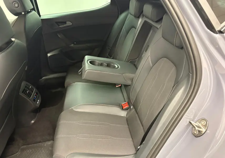 Vue côté droit de l'intérieur arrière gris foncé de la CUPRA Leon 2025 avec accoudoir central et porte ouverte.