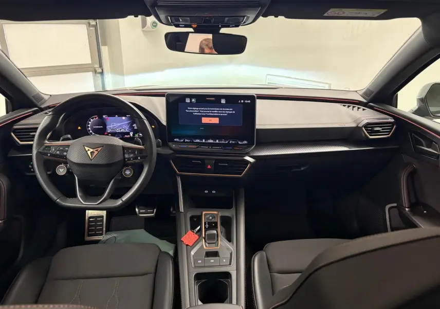 Vue intérieure avant du CUPRA Leon 2025, tableau de bord noir avec écran central tactile et volant multifonction au logo CUPRA.