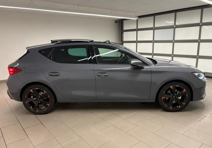 Vue de profil côté gauche d'une CUPRA Leon gris Graphène avec toit ouvrant panoramique et jantes cuivrées.