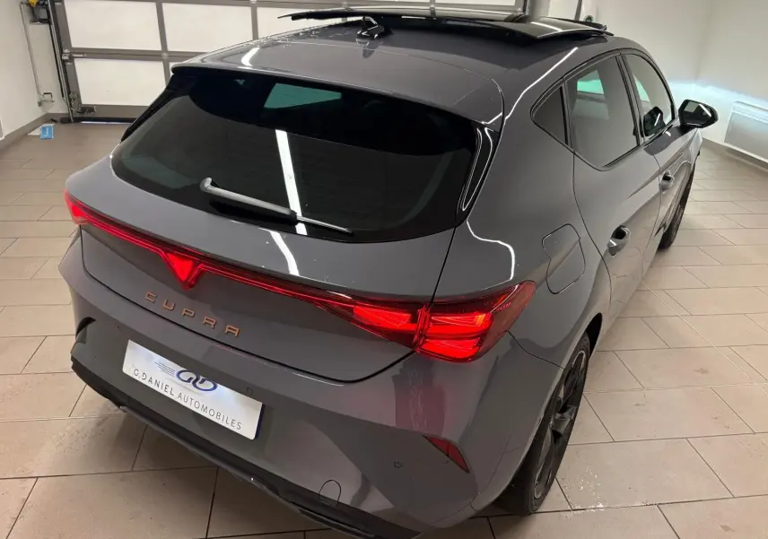 Vue 3/4 arrière droite d'une CUPRA Leon gris Graphène avec toit ouvrant panoramique et feux arrière LED allumés.