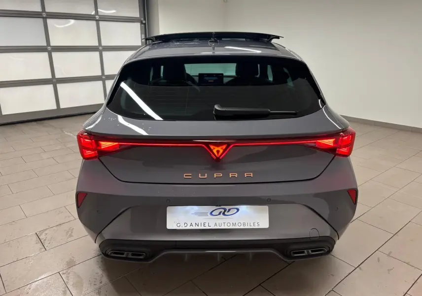 Vue arrière d'une CUPRA Leon gris Graphène avec feux LED allumés et toit ouvrant panoramique visible en intérieur showroom.