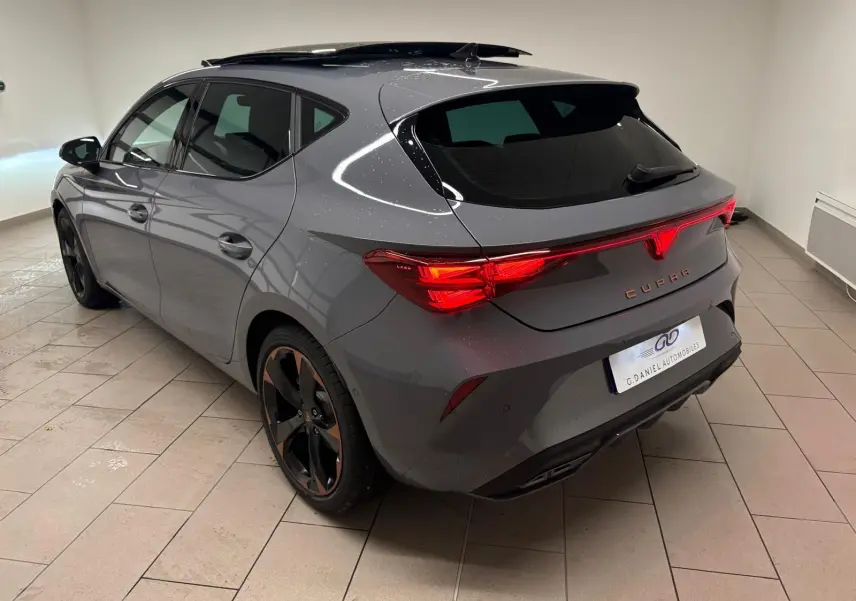 Vue 3/4 arrière droite d'une CUPRA Leon gris Graphène avec jantes cuivrées et toit ouvrant panoramique en intérieur.