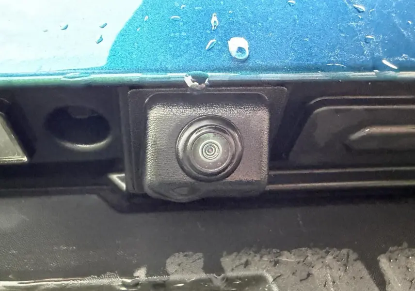 Gros plan sur la caméra de recul noire sous la peinture Bleu Zanzibar métallisée du hayon arrière du Renault Arkana 2025.