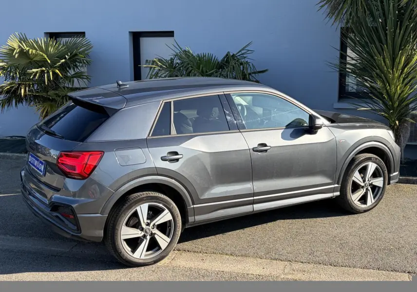 Audi Q2 gris Daytona en vue de profil côté droit, avec jantes alliage 18 pouces et vitres arrière surteintées.